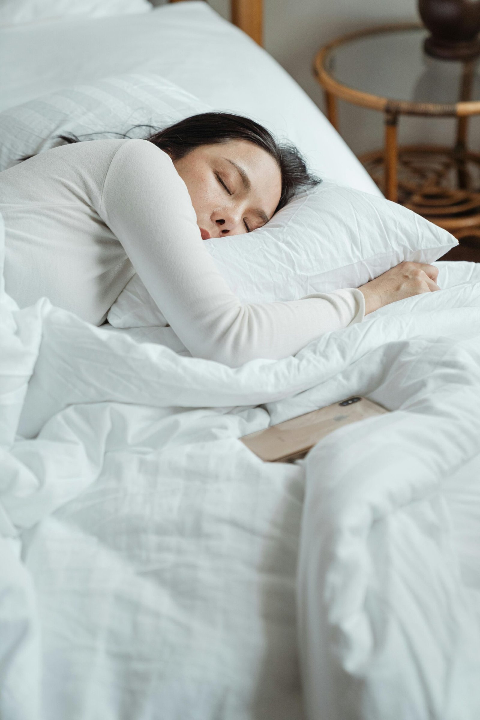 Woman in a cozy bedroom sleeping peacefully, surrounded by white bedding for ultimate comfort.